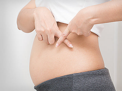 Frau mit leichtem Schwangerschaftsbauch zeigt Kreuz mit Zeigefinger