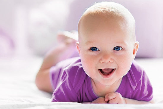 Lachendes Baby mit lila Oberteil und blauen Augen