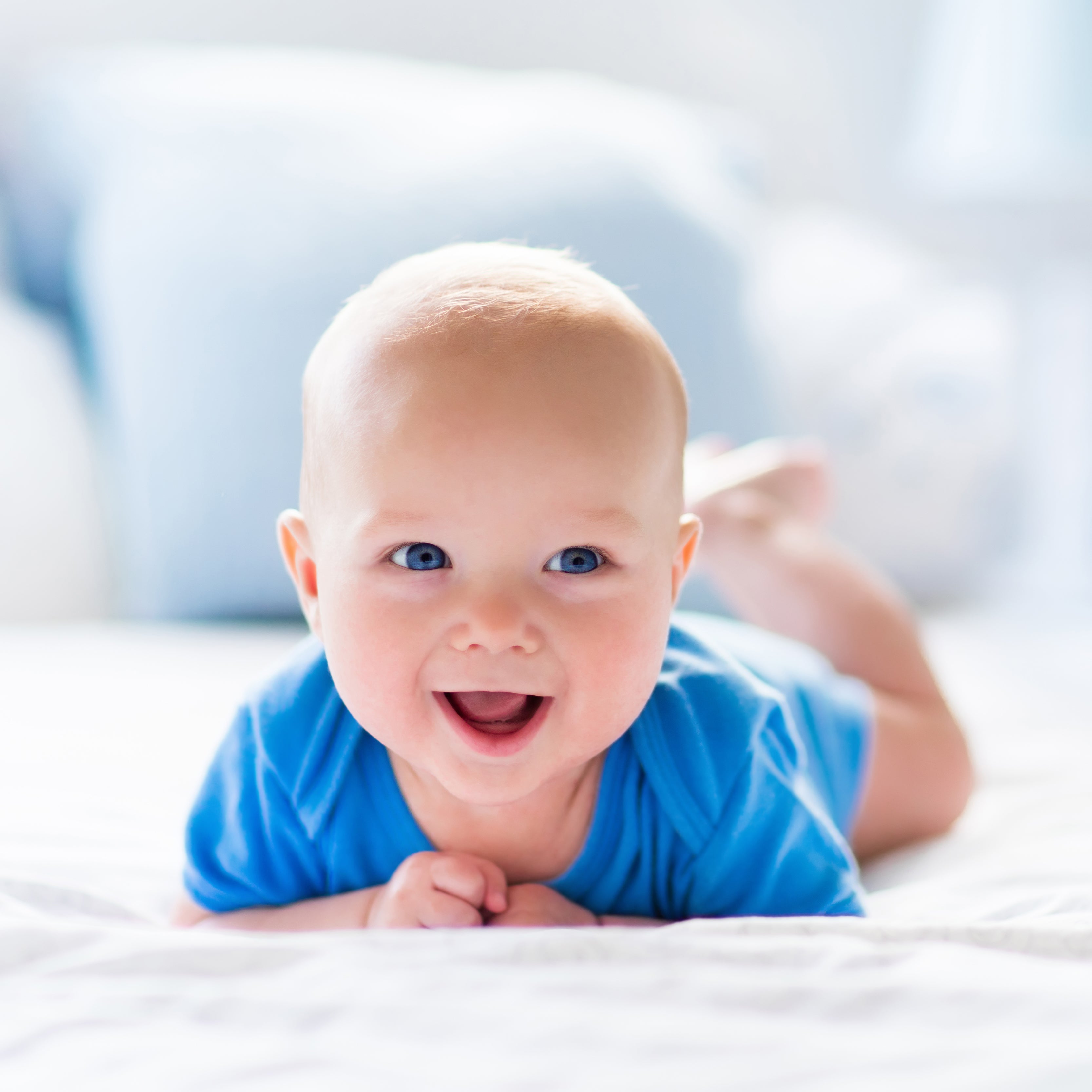Ein Baby liegt auf dem Bauch in blauer Kleidung und lächelt.