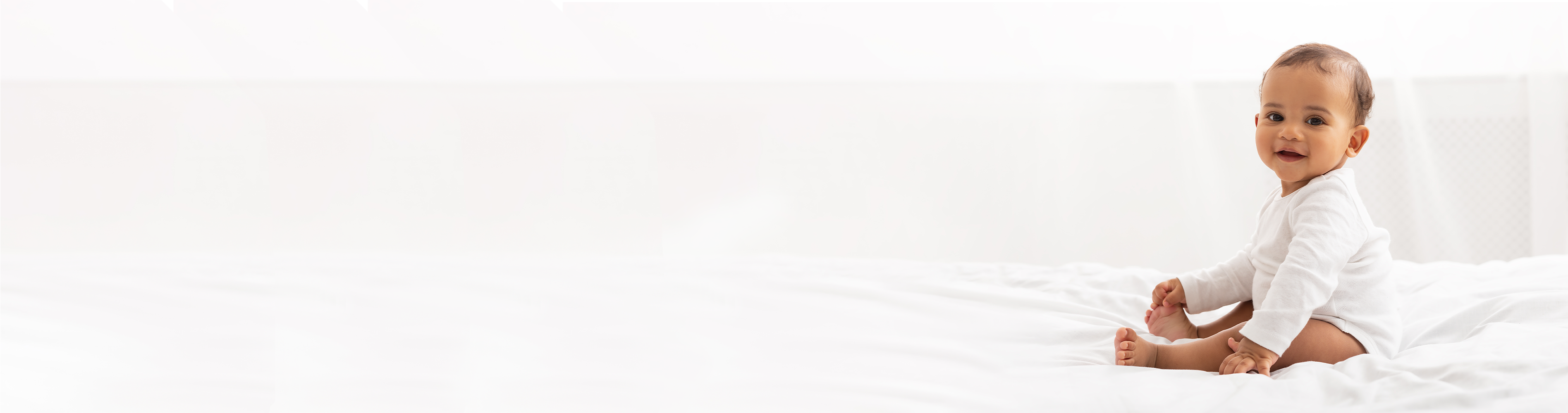 Banner Baby sitzt auf Bett und spielt mit seinen Füßen