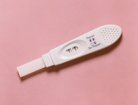 Positiver Schwangerschaftstest mit lachsfarbenem Hintergrund