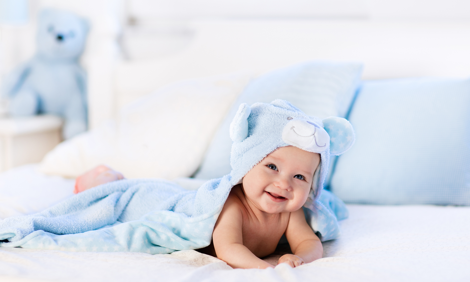 lachendes Baby liegt auf dem Bauch unter einer Decke und schaut rauf.
