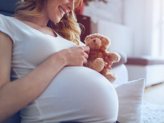 Schwangere Frau mit Teddybär in der Hand lächelt
